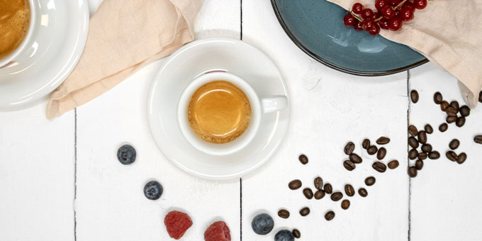 Espressotasse mit Früchten und Kaffeebohnen auf weißer Holzplatte