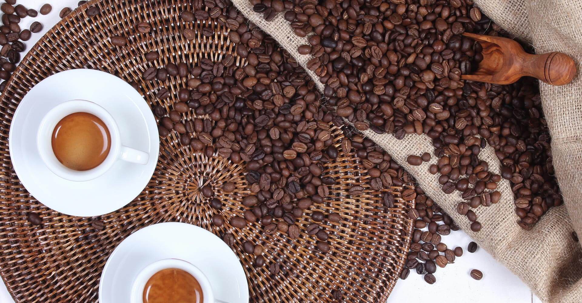 Kaffeebohnen kommen aus dem Kaffeesack, daneben stehen zwei fertige Espressi in weißen Espressotassen