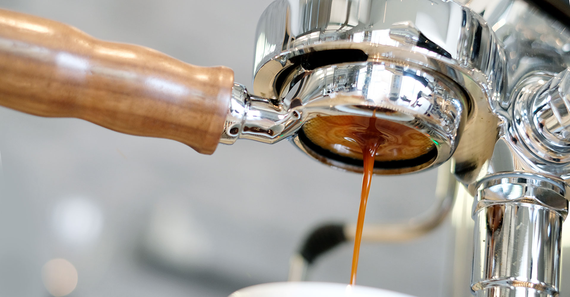 Der braune Espresso sammelt sich am bodenlosen Siebträger mit hellbraunem Holzgriff und läuft in eine Tasse